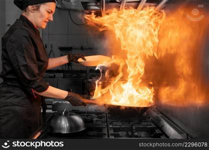 Woman Chef Cooking wok in the Kitchen. Cooking flaming wok with vegetables in the commercial kitchen. High quality photography.. Woman Chef Cooking wok in the Kitchen. Cooking flaming wok with vegetables in the commercial kitchen.