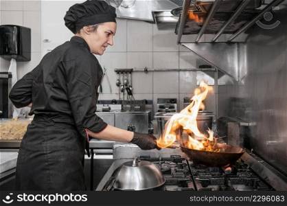 Woman Chef Cooking wok in the Kitchen. Cooking flaming wok with vegetables in the commercial kitchen. High quality photography.. Woman Chef Cooking wok in the Kitchen. Cooking flaming wok with vegetables in the commercial kitchen.