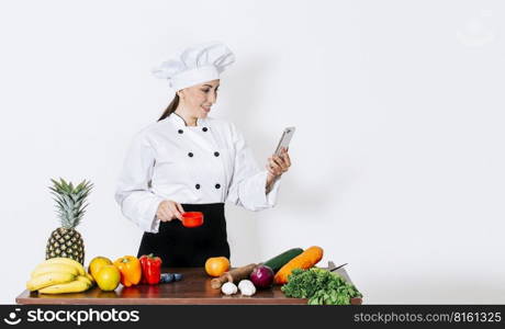 Woman chef with vegetables on the table looking for recipes with her smartphone. A woman chef in the kitchen looking for recipes with her cell phone, Chef people looking for cooking recipes