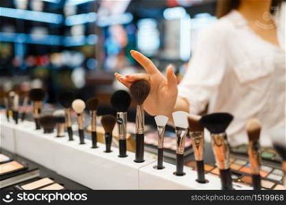 Woman choosing brush at the shelf in cosmetics store. Buyer at the showcase in luxury beauty shop salon, female customer in fashion market. Woman choosing brush at shelf in cosmetics store