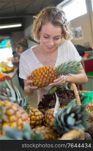 woman choosing fruits at supermarket and holding pineapple