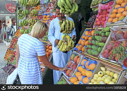 Woman choosing fruits in tray from street vendor. Woman tourist buying fruits at street seller. Girl buying mangoes, pomegranates, bananas, plums, guava, oranges. Fresh fruits in shop. Woman tourist buying fruits at street seller. mangoes, pomegranates, guava,