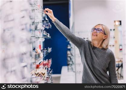 Woman choosing glasses at optic store. Correction eyewear, eyesight defect.. Woman choosing glasses at optic store.
