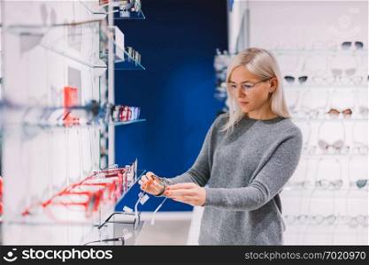 Woman choosing glasses at the optics, shopping for correction eyewear. Ophthalmology.. Woman choosing glasses at optics.
