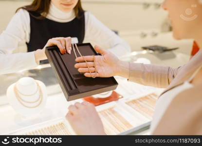 Woman choosing golden chain in jewelry store. Female person buying gold decoration in jewellery shop. Woman choosing golden chain in jewelry store