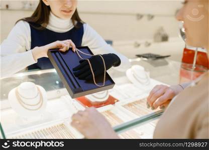 Woman choosing golden chain in jewelry store. Female person buying gold decoration in jewellery shop