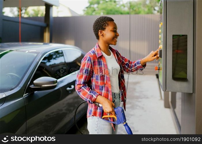Woman choosing program on water gun, car wash station. Carwash industry or business. Female person cleans her vehicle from dirt outdoors. Woman choosing program on car wash station