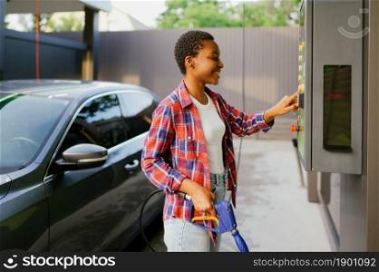 Woman choosing program on water gun, car wash station. Carwash industry or business. Female person cleans her vehicle from dirt outdoors. Woman choosing program on car wash station