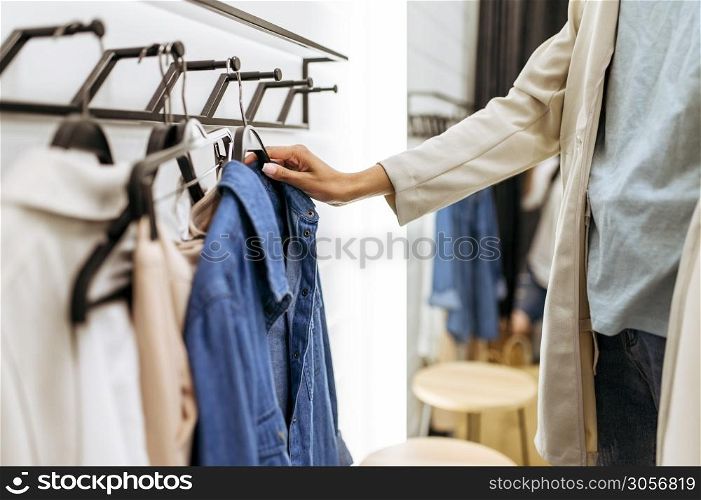 Woman choosing shirt in clothing store. Female person shopping in fashion boutique, shopaholic, shopper looking on clothes. Woman choosing shirt in clothing store