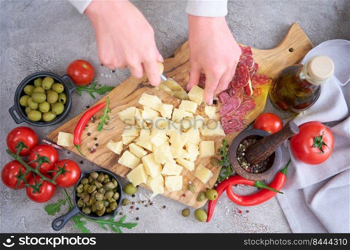 Woman chopping Parmesan cheese with knife on grey table at domestic kitchen.. Woman chopping Parmesan cheese with knife on grey table at domestic kitchen