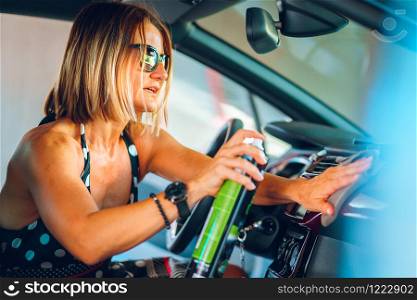 Woman cleaning her car cockpit using spray and microfiber cloth to clean and shine dashboard at self service car wash garage