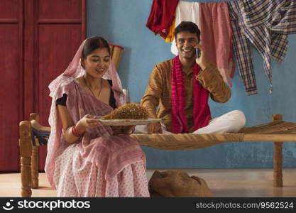 Woman cleaning paddy seeds at home while her husband talking on mobile phone