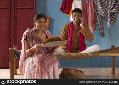 Woman cleaning paddy seeds at home while her husband talking on mobile phone