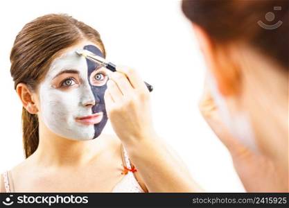 Woman cleaning skin face, using green mud and carbo black mask. Girl taking care of oily complexion. Beauty and kincare.. Girl black and green mud mask on face