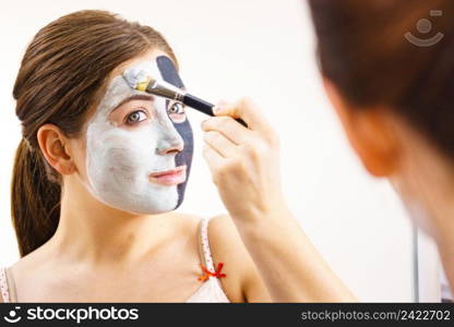 Woman cleaning skin face, using green mud and carbo black mask. Girl taking care of oily complexion. Beauty procedures. Skincare.. Girl black and green mud mask on face
