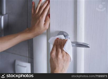 Woman cleaning the door handle with disinfecting wipe