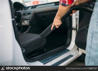 Woman cleans car interior with vacuum cleaner, carwash. Lady with hoover on self-service automobile washing. Outdoor vehicle cleaning. Woman cleans car interior with vacuum cleaner