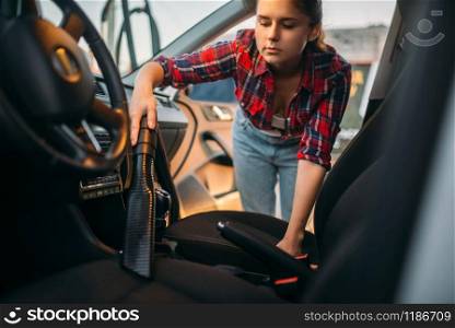 Woman cleans car interior with vacuum cleaner, carwash. Lady with hoover on self-service automobile washing. Outdoor vehicle cleaning at summer day