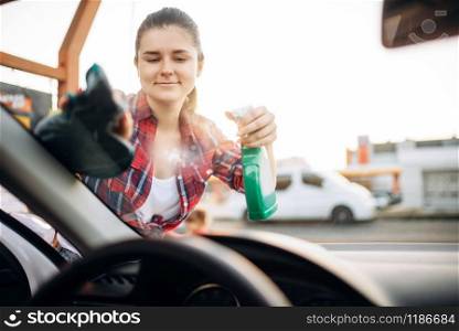 Woman cleans the windshield of the car with spray, view from the inside, carwash. Lady on self-service automobile washing. Outdoor vehicle cleaning at summer day