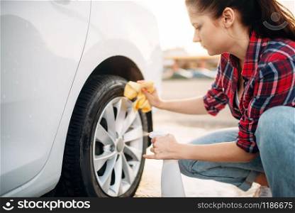 Woman cleans wheel disk of the car with spray, carwash. Lady on self-service automobile washing. Outdoor vehicle cleaning at summer day. Woman cleans wheel disk of the car with spray