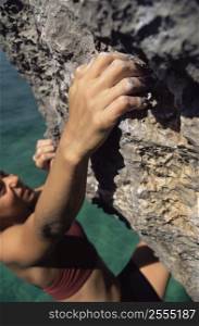 Woman climbing rocks in swimwear by ocean (selective focus)