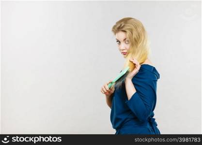 Woman combing her hair with brush. Young female with beautiful natural blond straight long hairs, studio shot on grey. Woman brushing her long hair with brush
