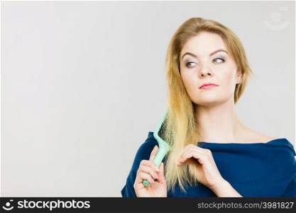 Woman combing her hair with brush. Young female with beautiful natural blond straight long hairs, studio shot on grey. Woman brushing her long hair with brush