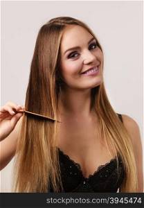 Woman combing her long hair with wooden comb. Woman wearing lace lingerie refreshing her hairstyle combing long hair with wooden comb. Health beauty and haircare concept