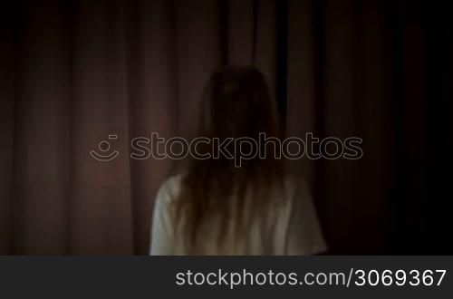 Woman coming to the window in the morning, opening curtains and stretching out in sunlight