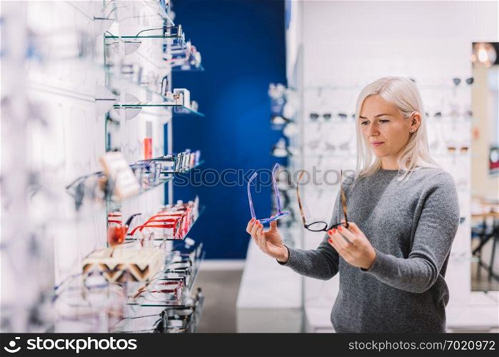 Woman comparing glasses at optic store. Eyewear shopping, correction glasses.. Woman comparing glasses at optic store.