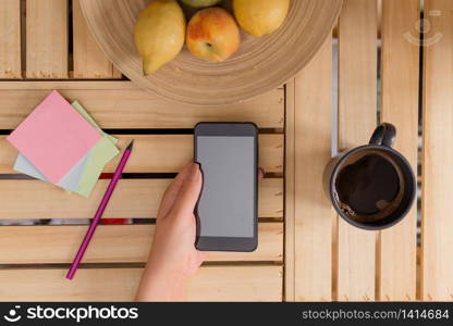 woman computer smartphone drink mug office supplies technological devices. Young lady using and holding a dark smartphone in a crate table with a mug of black coffee. Office supplies, cell phone, technological devices and wooden desk.
