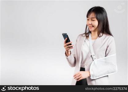 Woman confident smiling broken arm after accident and wear arm splint for treatment and hold smartphone, happy Asian female sling supported hand isolated on white background, social media, copy space