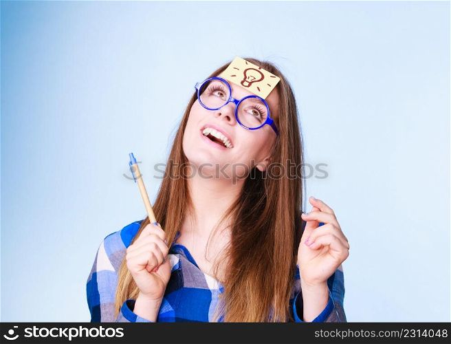 Woman confused thinking seeks a solution, paper card with light idea bulb on her head. Excited girl with many ideas celebrates success. Eureka creativity concept studio shot on blue.. woman thinking light idea bulb on head, creative girl lots of ideas