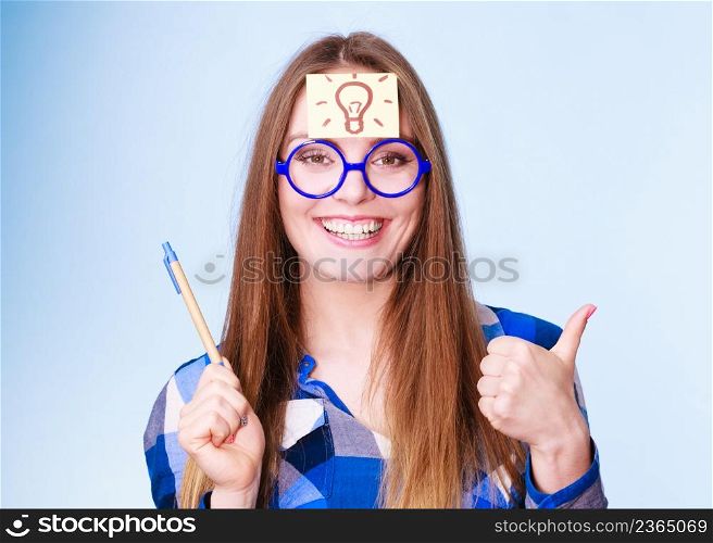 Woman confused thinking seeks a solution, paper card with light idea bulb on her head. Excited girl with many ideas celebrates success. Eureka creativity concept studio shot on blue.. woman thinking light idea bulb on head, creative girl lots of ideas