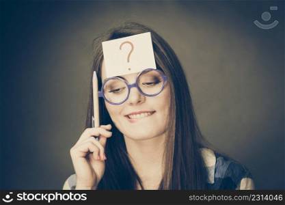Woman confused thinking seeks a solution, paper card with question mark on her head. Doubtful young female in glasses studio shot on black. woman thinking question mark on her head