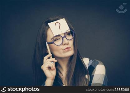 Woman confused thinking seeks a solution, paper card with question mark on her head. Doubtful young female in glasses studio shot on black. woman thinking question mark on her head