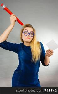 Woman confused thinking seeks a solution. Thoughtful student girl or business coach female teacher coming up with an idea, holding huge red pencil and note paper. Studio shot on grey. Confused woman holds big pencil note paper in hand