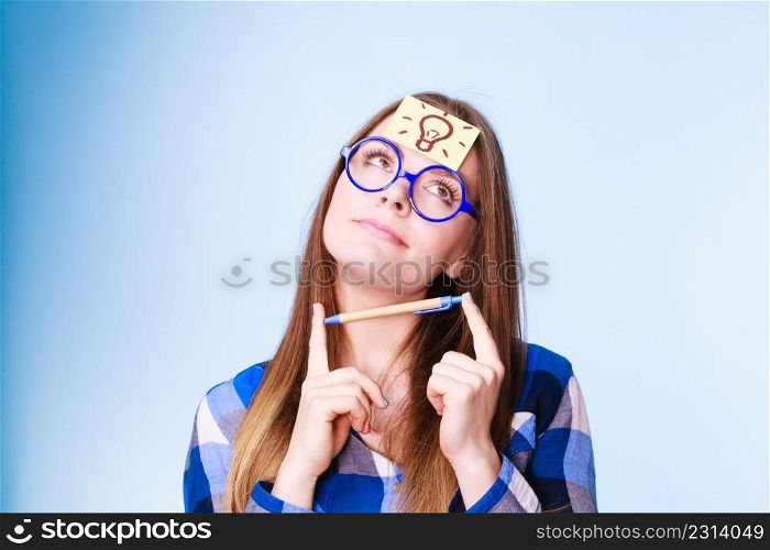 Woman confused thinking seeks solution, paper card with light idea bulb on her head. Girl is trying to create a new idea for some business project or case study studio shot on blue. woman thinking light idea bulb on head