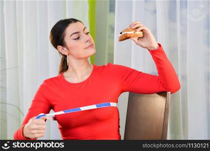 Woman considers eating a sandwich while using a measuring tape on an out of focus background. Healthy lifestyle concept.. Woman considers taking a bite of a sandwich