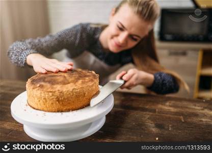 Woman cook cut fresh baked cake with a knife. Kitchen on background. Homemade dessert