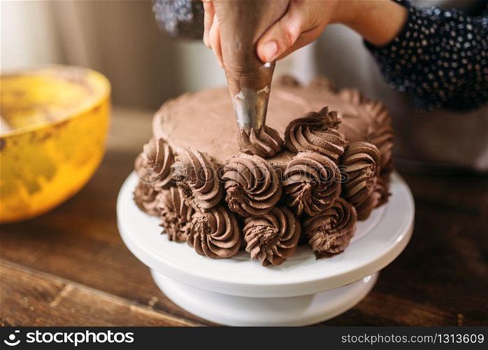 Woman cook decorate chocolate cake with culinary syringe. Kitchen on background. Homemade dessert decoration. Woman decorate cake with culinary syringe