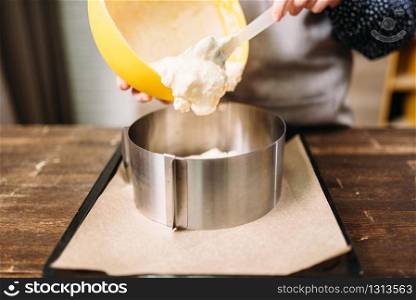 Woman cook in apron adds cream for the cake into the pan. Kitchen on background. Woman cook adds cream for the cake into the pan