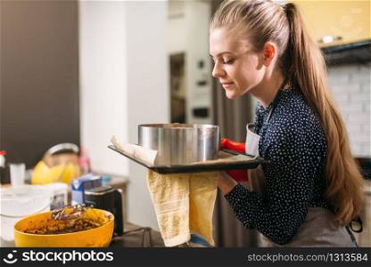 Woman cook in apron holds hot pan with fresh cake. Kitchen on background. Homemade dessert
