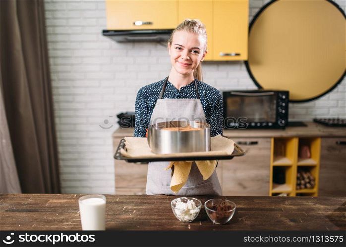 Woman cook in apron holds pan with fresh cake. Kitchen on background. Homemade dessert. Woman cook in apron holds pan with fresh cake