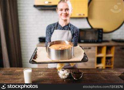 Woman cook in apron holds pan with fresh cake. Kitchen on background. Homemade dessert