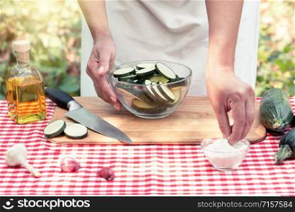 Woman cook salt sliced zucchini. Checkered tablecloth on the table, natural green background. The concept of cooking natural eco-friendly dishes. Woman cook salt sliced zucchini