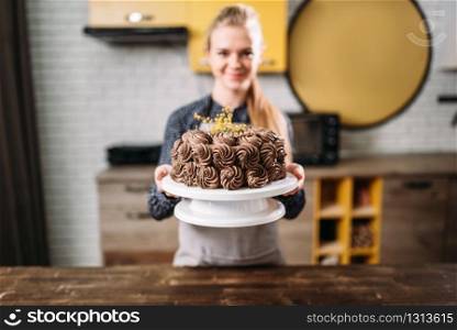 Woman cook shows chocolate cake, culinary masterpiece. Kitchen on background. Homemade sweet dessert