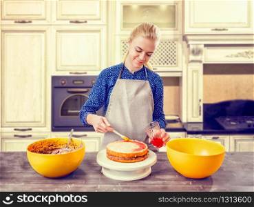 Woman cook smears baked cake with berry jam. Tasty dessert homemade cooking