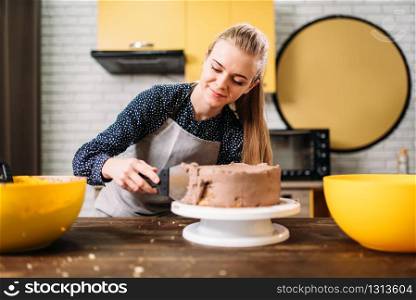 Woman cook smears baked cake with chocolate cream. Tasty dessert preparation. Homemade cooking