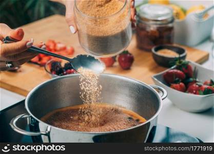 Woman cooking fruits and making homemade jam. Putting brown sugar in the pot.. Woman Preparing Fruits, Making Jam.